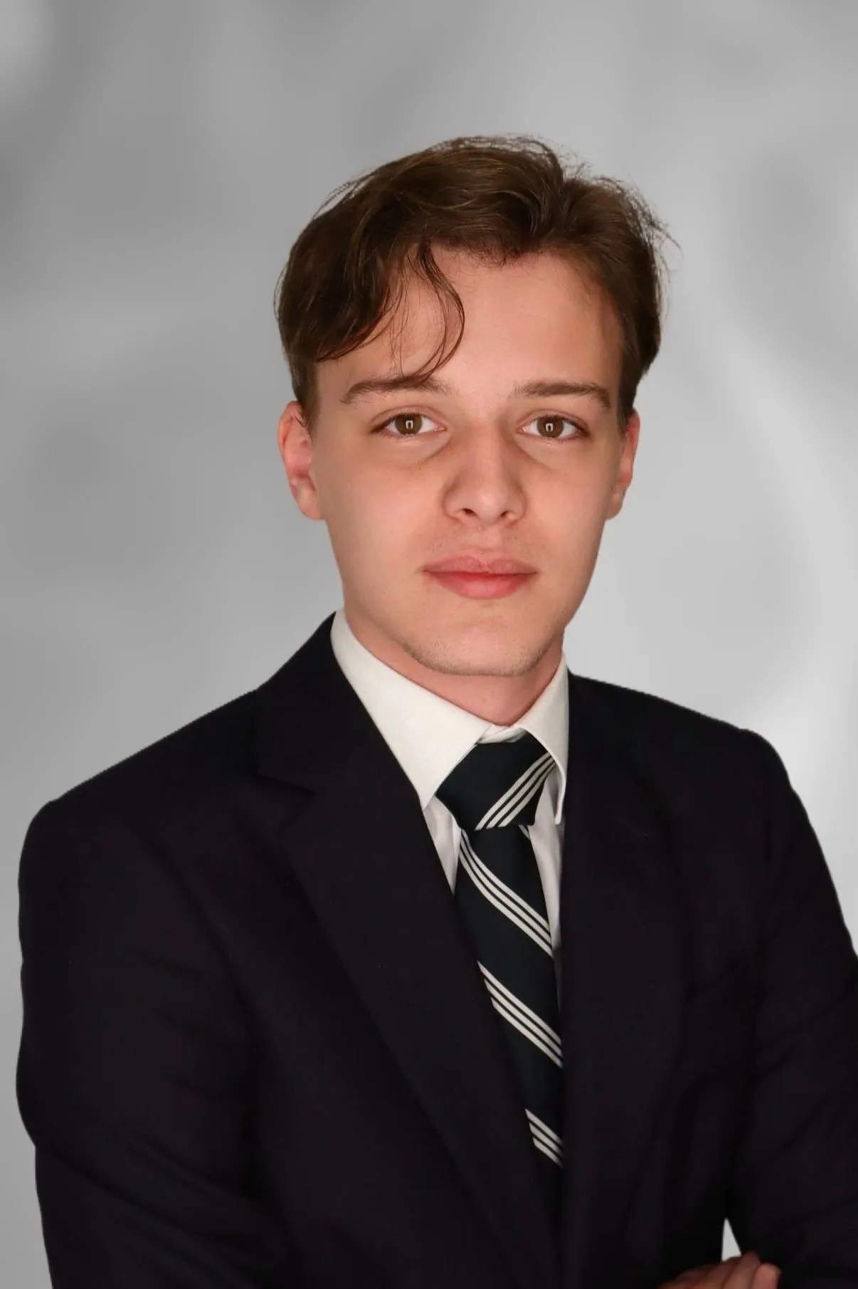 An individual wearing a white shirt, sport coat, and tie, posing for a portrait.